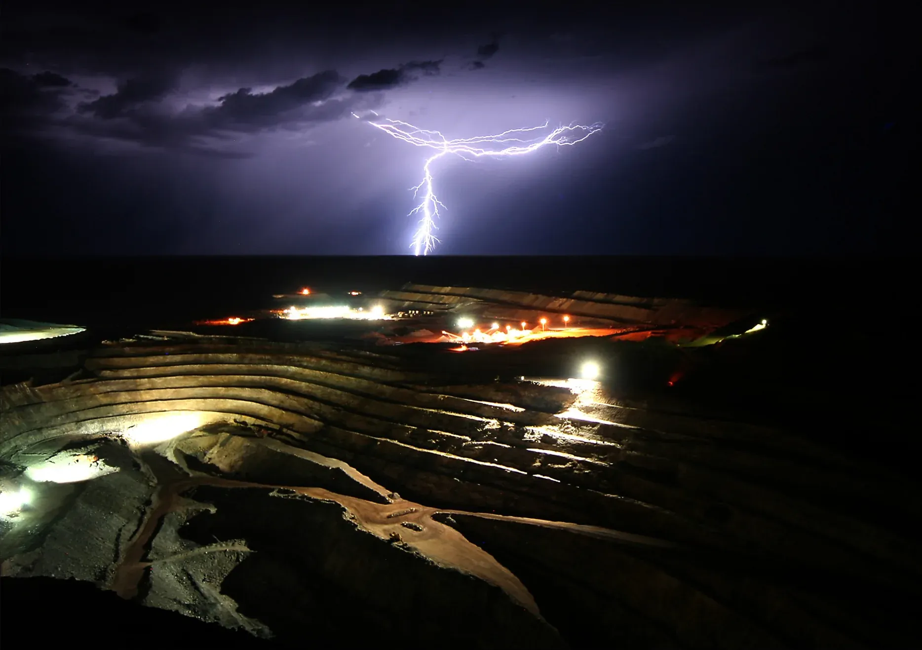 Open pit mine at night during a lightning storm